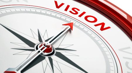 Arrow of a compass is pointing vision text on the compass. Arrow , vision text and the frame of compass are metallic red in color. White background. Horizontal composition with copy space. Vision concept.